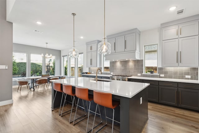 kitchen with a sink, tasteful backsplash, light countertops, a center island with sink, and a breakfast bar area