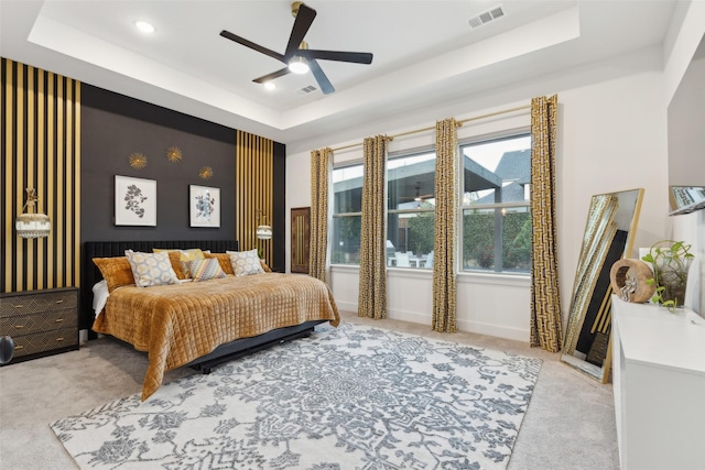 bedroom featuring a tray ceiling, light carpet, baseboards, and a ceiling fan
