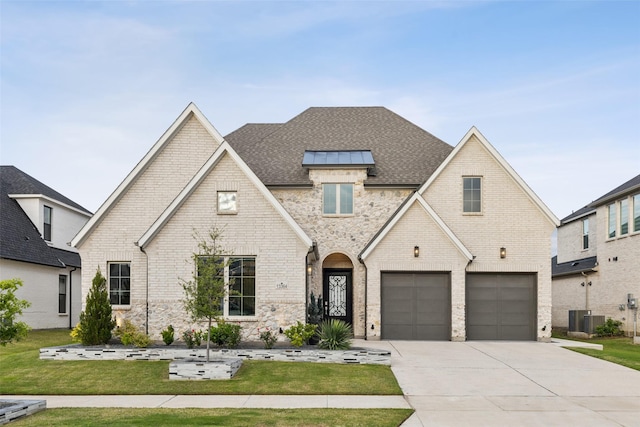 french country style house featuring a garage, driveway, a front lawn, a shingled roof, and brick siding