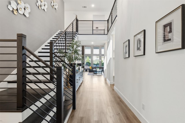 hall featuring stairway, baseboards, wood finished floors, and a high ceiling