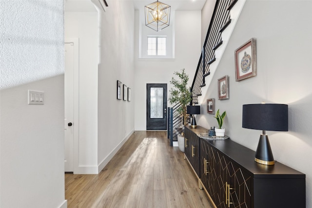 entrance foyer featuring light wood-style floors, a chandelier, baseboards, a high ceiling, and stairway
