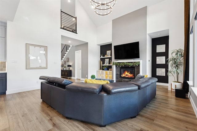 living room featuring a high ceiling, light wood-style floors, stairway, a glass covered fireplace, and baseboards