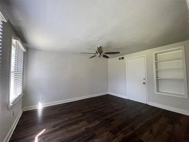 empty room with a ceiling fan, dark wood-type flooring, plenty of natural light, and a textured ceiling