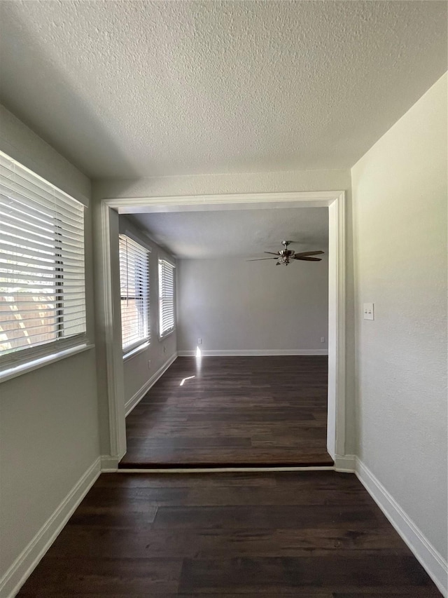 hallway with a textured ceiling, wood finished floors, and baseboards