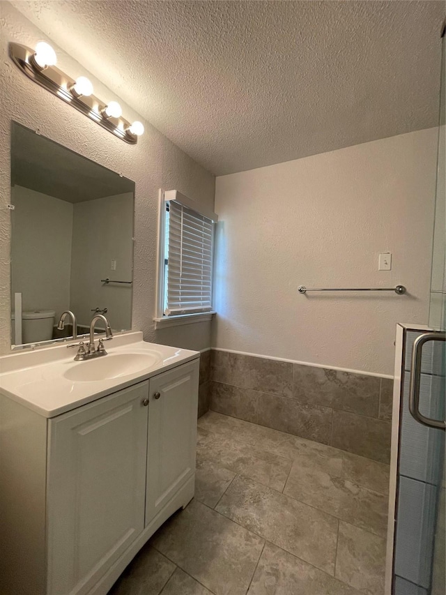 full bath with a textured ceiling, vanity, a wainscoted wall, tile patterned floors, and toilet