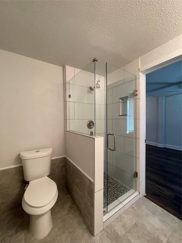 full bath with a shower stall, toilet, and a textured ceiling