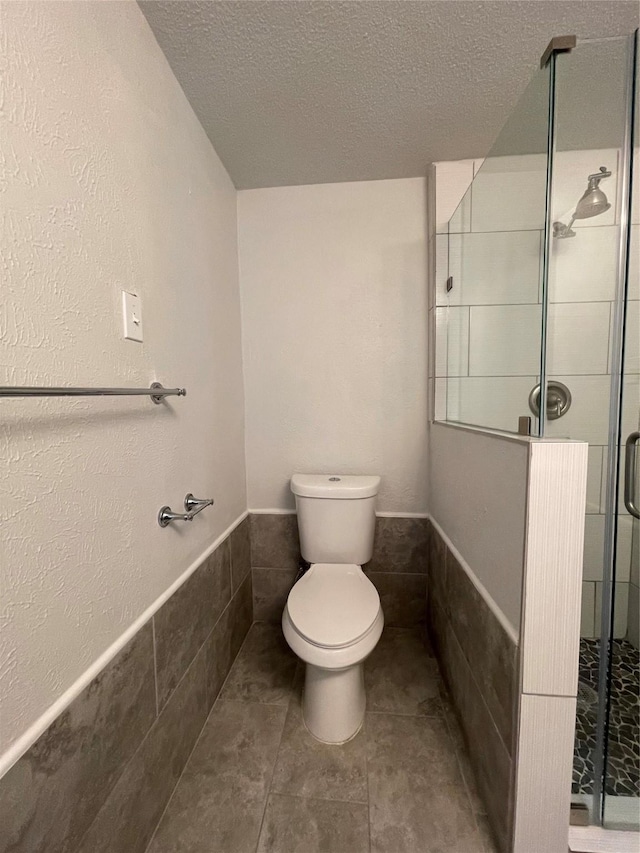 bathroom featuring toilet, a stall shower, wainscoting, and a textured ceiling