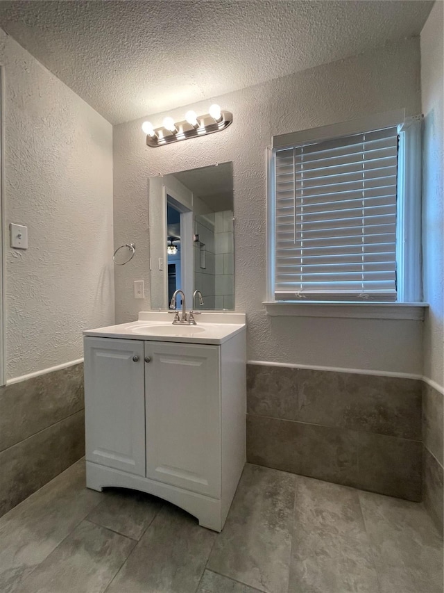 bathroom with a textured ceiling, vanity, a wainscoted wall, a textured wall, and tile patterned floors