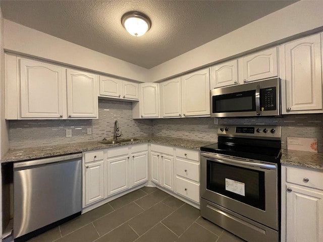 kitchen featuring appliances with stainless steel finishes, a sink, stone countertops, dark tile patterned floors, and a textured ceiling