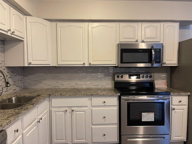 kitchen with stainless steel appliances, a sink, decorative backsplash, and white cabinetry