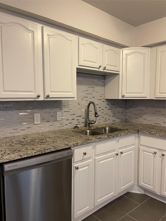 kitchen featuring stainless steel dishwasher, a sink, dark tile patterned floors, and white cabinets