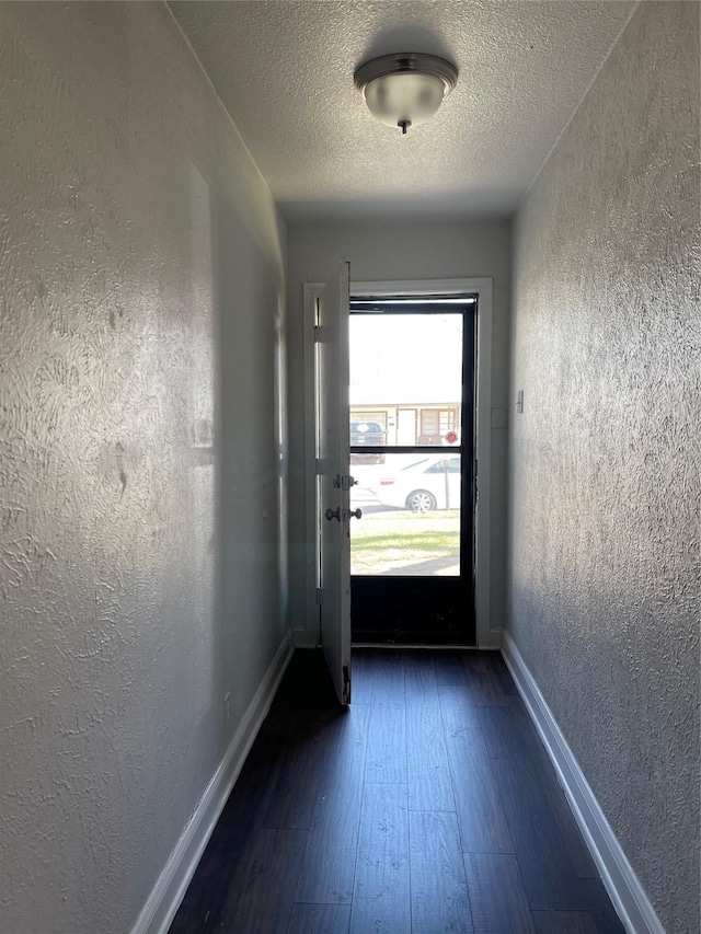 entryway with a textured ceiling, a textured wall, dark wood-style flooring, and baseboards