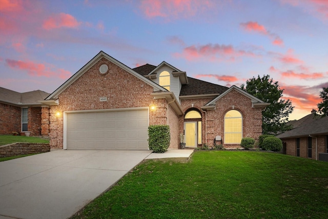 traditional-style house with brick siding, driveway, a front yard, an attached garage, and roof with shingles