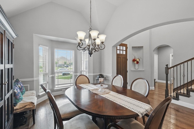 dining area featuring arched walkways, a chandelier, stairway, wood finished floors, and baseboards