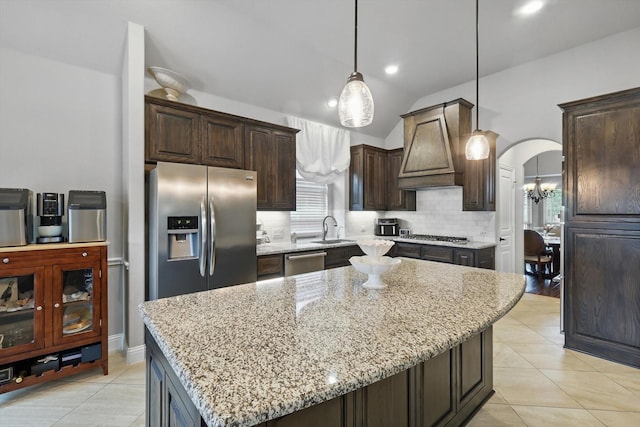 kitchen with appliances with stainless steel finishes, a sink, decorative backsplash, lofted ceiling, and light stone countertops