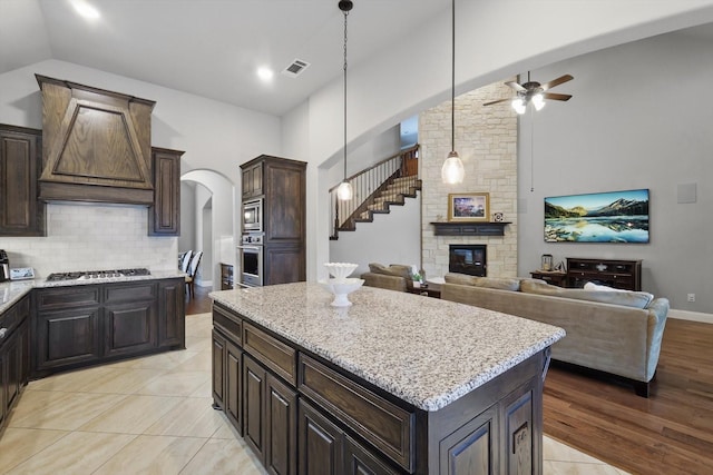 kitchen with stainless steel appliances, a ceiling fan, tasteful backsplash, light stone countertops, and premium range hood