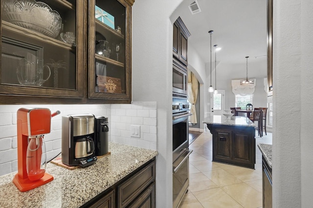 kitchen with dark brown cabinets, arched walkways, stainless steel microwave, and light stone counters