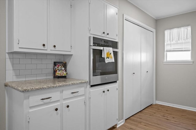 3205 Creekwood Cir, Waco, TX 76710 - kitchen with stainless steel oven, backsplash, white cabinetry, light wood finished floors, and baseboards