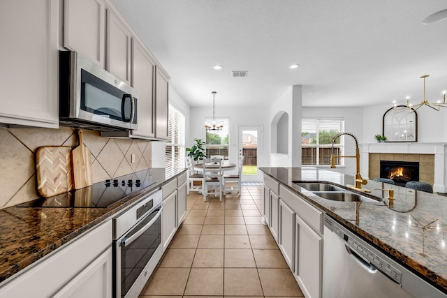 kitchen featuring appliances with stainless steel finishes, a sink, a chandelier, light tile patterned floors, and healthy amount of natural light