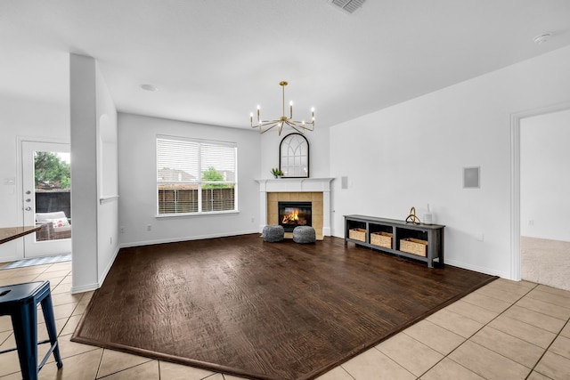 unfurnished living room with a chandelier, healthy amount of natural light, light tile patterned flooring, and a tiled fireplace