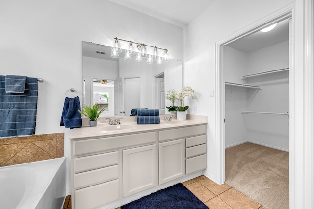 bathroom with a walk in closet, a garden tub, ceiling fan, vanity, and tile patterned flooring