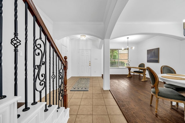 entryway featuring arched walkways, ornamental molding, light tile patterned flooring, stairway, and a chandelier