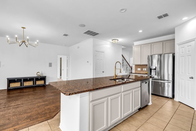 kitchen featuring stainless steel appliances, a sink, light tile patterned floors, a chandelier, and dark stone counters