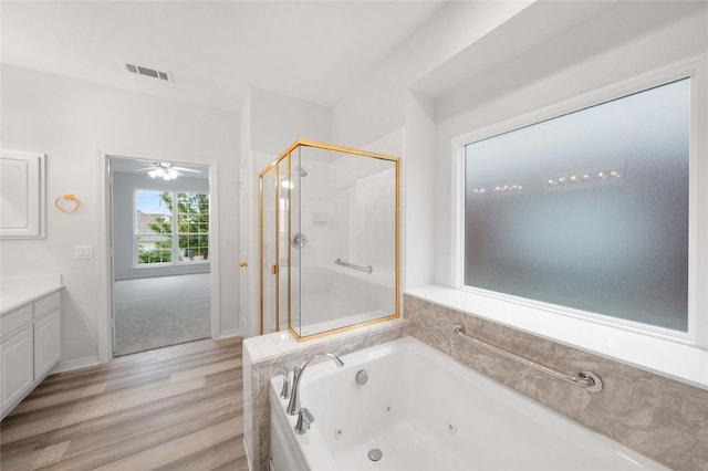 full bathroom featuring a stall shower, a tub with jets, wood finished floors, vanity, and ceiling fan