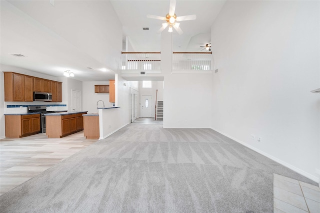 kitchen with open floor plan, appliances with stainless steel finishes, a ceiling fan, light carpet, and a towering ceiling