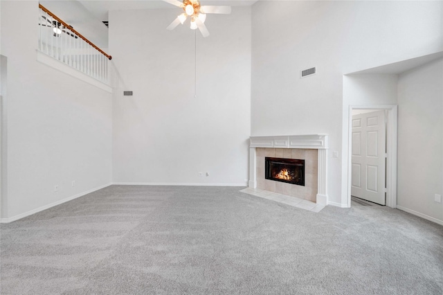 unfurnished living room featuring a high ceiling, carpet floors, ceiling fan, a tiled fireplace, and baseboards