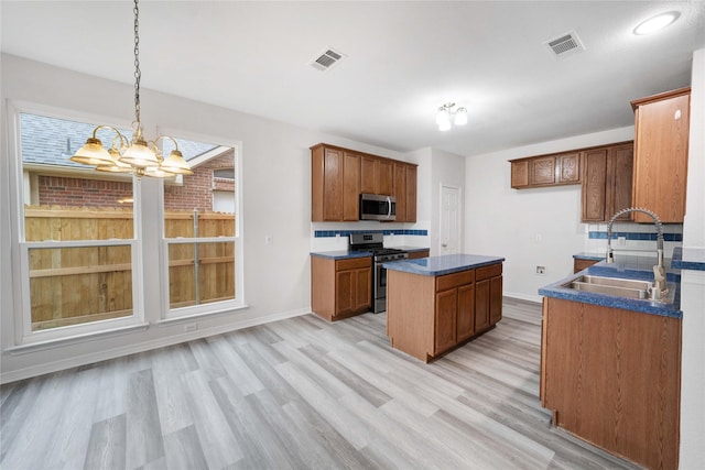 kitchen featuring appliances with stainless steel finishes, a sink, dark countertops, light wood-type flooring, and a chandelier