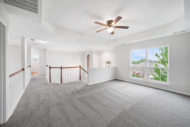 carpeted empty room featuring ceiling fan, a tray ceiling, and baseboards