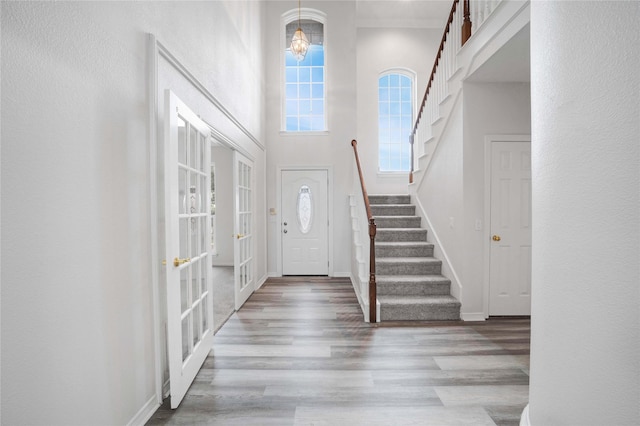 foyer entrance with stairway, wood finished floors, baseboards, a towering ceiling, and french doors