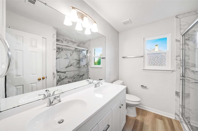 full bath featuring a marble finish shower, toilet, wood finished floors, double vanity, and baseboards