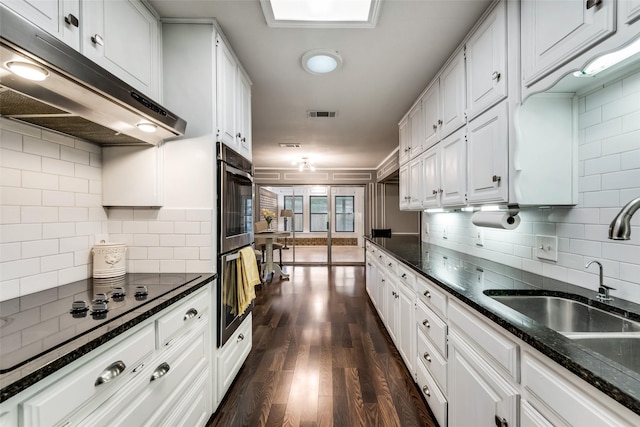 kitchen featuring under cabinet range hood, white cabinetry, a sink, dark wood finished floors, and tasteful backsplash