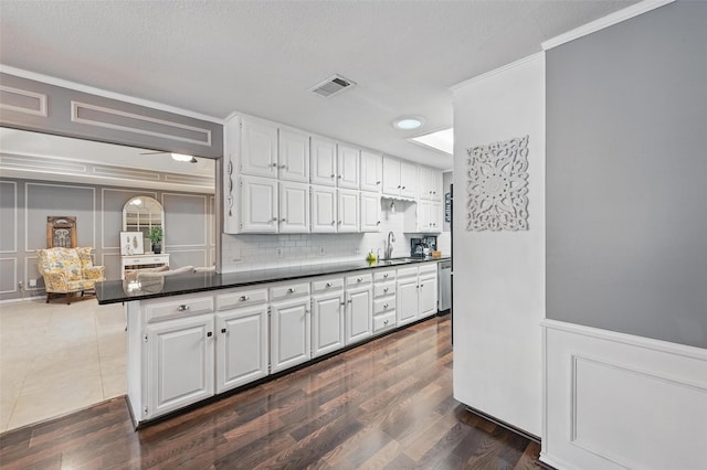 kitchen featuring dark countertops, a decorative wall, white cabinetry, ornamental molding, and a sink