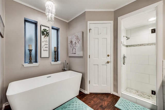 bathroom featuring wood finished floors, ornamental molding, a shower stall, a freestanding tub, and baseboards
