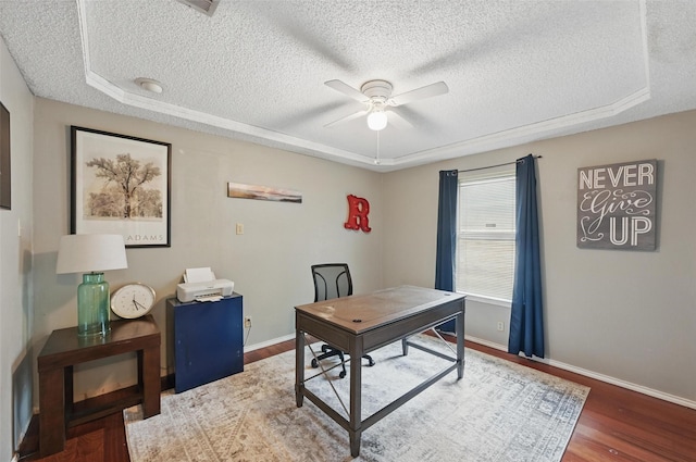 home office featuring a textured ceiling, a raised ceiling, ceiling fan, baseboards, and wood finished floors