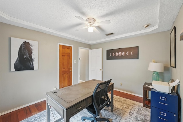 office space with a textured ceiling, wood finished floors, baseboards, ceiling fan, and a raised ceiling