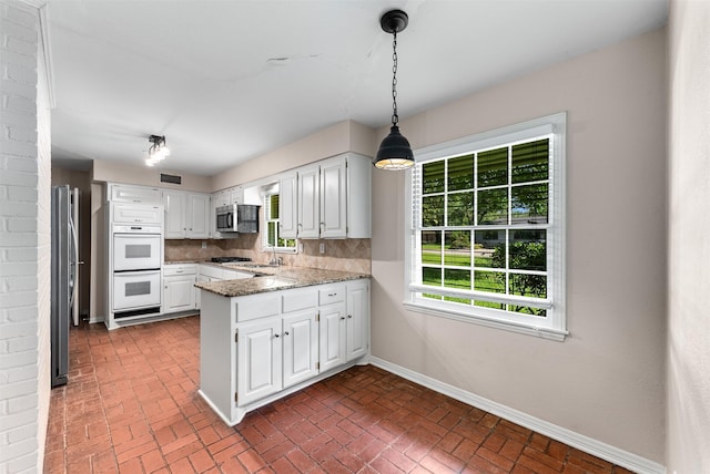 6838 Lupton Dr, Dallas, TX 75225 - kitchen with stainless steel appliances, a peninsula, baseboards, brick floors, and white cabinetry