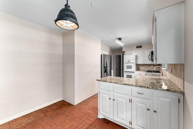 6838 Lupton Dr, Dallas, TX 75225 - kitchen featuring appliances with stainless steel finishes, brick floors, baseboards, a sink, and white cabinetry