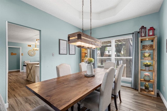 7012 Fox Dr, The Colony, TX 75056 - dining space with wood finished floors, baseboards, a chandelier, a textured ceiling, and a raised ceiling