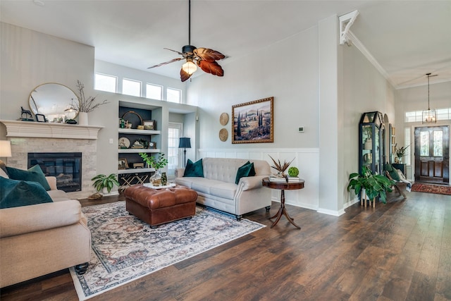 living room with a high ceiling, healthy amount of natural light, a ceiling fan, a glass covered fireplace, and dark wood finished floors