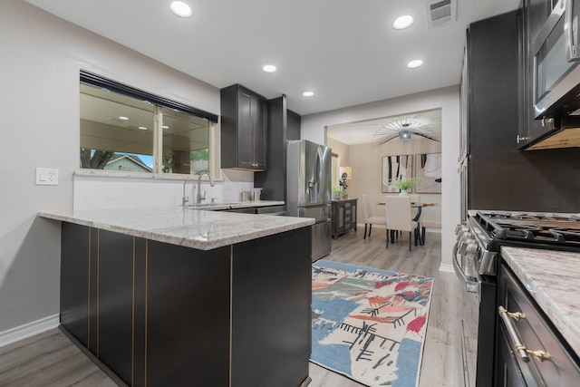3809 Runge Ct E, Irving, TX 75038 - kitchen with stainless steel appliances, a sink, light wood-style floors, light stone counters, and a peninsula