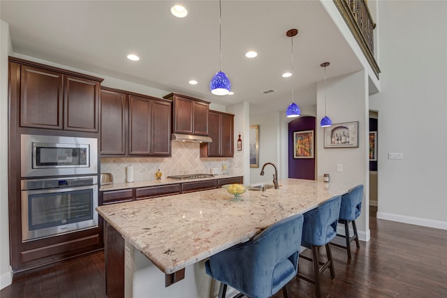 4458 Hartebeest Trl, Frisco, TX 75034 - kitchen with appliances with stainless steel finishes, under cabinet range hood, dark wood-style flooring, baseboards, and a kitchen bar