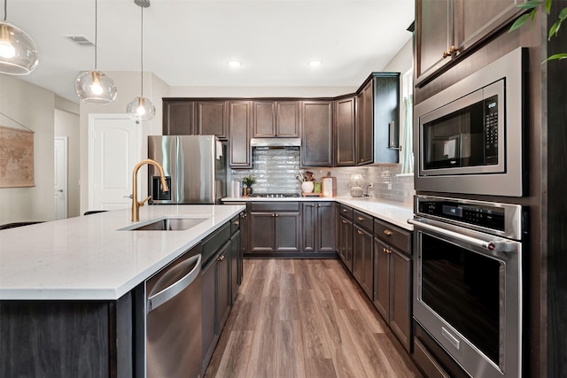 kitchen featuring appliances with stainless steel finishes, a sink, light wood-style floors, dark brown cabinets, and under cabinet range hood