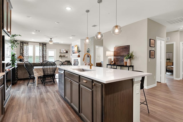 kitchen with a sink, light wood-style floors, a ceiling fan, light countertops, and open floor plan