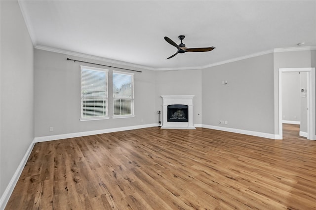 unfurnished living room featuring ceiling fan, crown molding, wood finished floors, baseboards, and a fireplace with raised hearth