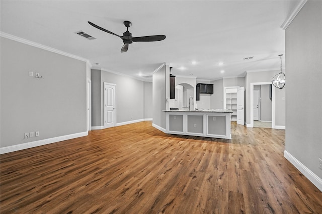 unfurnished living room featuring a sink, ceiling fan, wood finished floors, baseboards, and crown molding