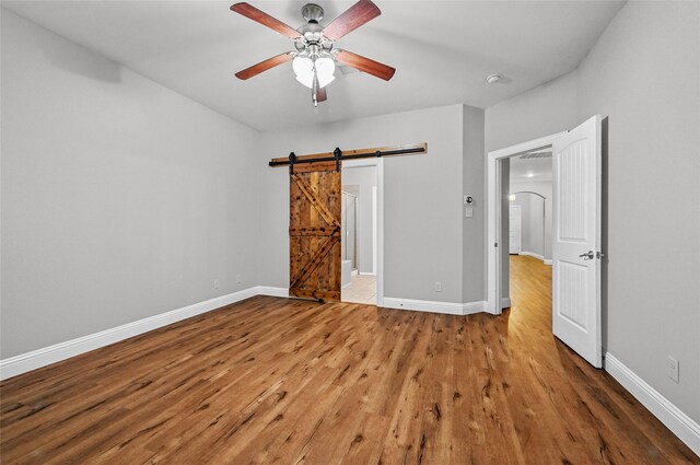 unfurnished bedroom featuring wood finished floors, baseboards, a ceiling fan, and a barn door
